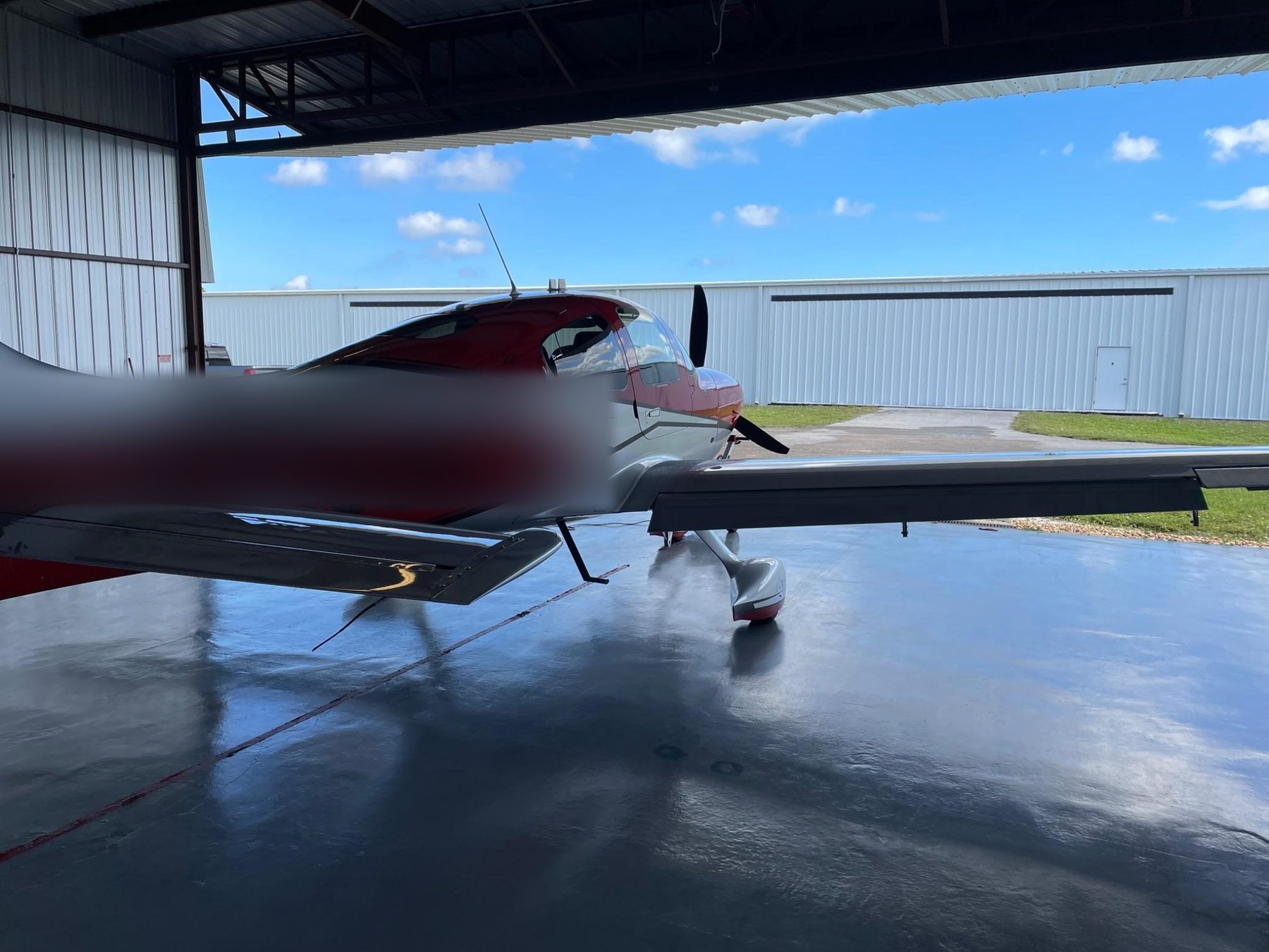 Red Cirrus parked at open hangar door